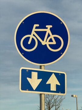 Blue road sign indicating a bike, Bike path road sign. Traffic sign white bicycle on blue circle against the backdrop of trees and sky. Concept of infrastructure development for ecological transport.