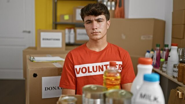 Young hispanic teenage volunteer with serious face sits at a table in charity center, showing true community service
