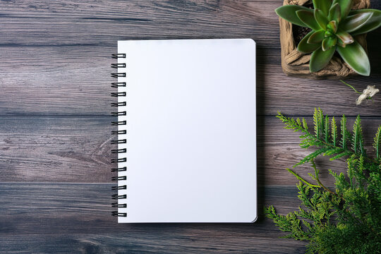 Spiral Notebook with White Pages and Green Plants on Wooden Texture