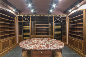 A room of a home wine cellar with wooden shelves and a table with a granite countertop in the...