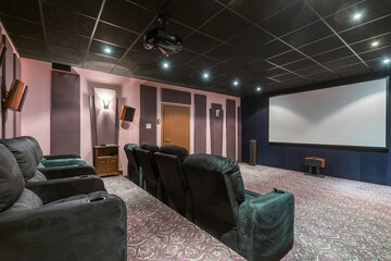 A luxurious home theater hall with a dark ceiling, a wide screen and comfortable gray armchairs.