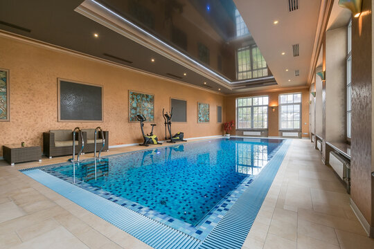 A large swimming pool, decorated with light blue tiles, in a private house. Mirror on the .ceiling.