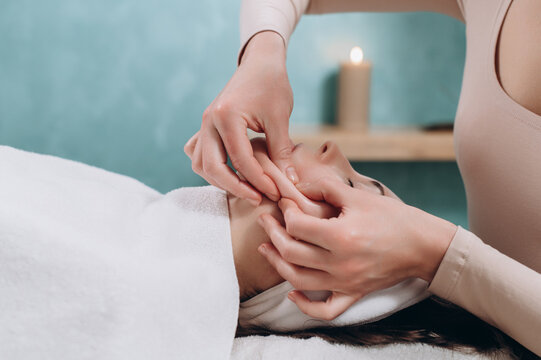 The beautician makes a deep facial massage to a young woman. Face massage technique against aging. Close-up.