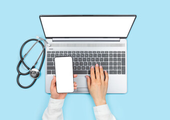 Female doctor's hands holding smartphone with blank screen and using laptop with empty monitor on blue background. Telemedicine concept