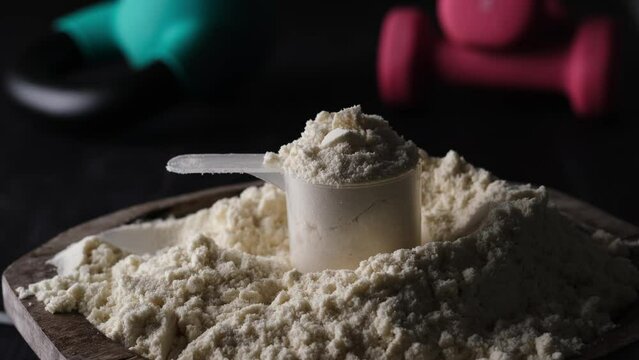 Focusing on a measuring spoon with whey protein powder, kettlebell and dumbbells, sport food and supplements