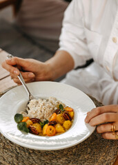 Close-up of a woman having breakfast, oatmeal with fruit and nuts on a white plate.