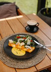 Omelette with cheese and salad on a plate, with a cup of coffee, on a wooden table at cafe terrace.