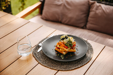 Waffles with salmon and vegetables, served with a glass of water, placed on a wooden table at a...