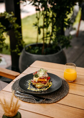 Waffle sandwich with ham, vegetables and cheese, served with orange juice, placed on a wooden table at a terrace on a summer day.