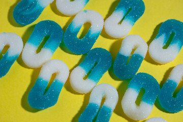 array of several lines of 0 shaped white and blue gummy candies on a yellow background,  horizontal...