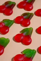vegan cherry gummies laying in a grid disposition on a pastel orange surface with harsh light. 45 degree diagonal  view