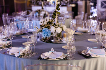 An elegantly set wedding reception table in blue tones with plates, glasses and textile handkerchiefs.
