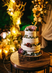 A three-tiered wedding cake adorned with fresh flowers and greenery, set against a backdrop of warm candlelight.