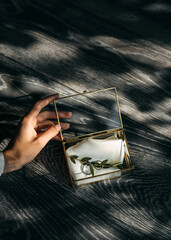 An elegant hand opens a glass box revealing wedding rings on a silk cloth with light casting...