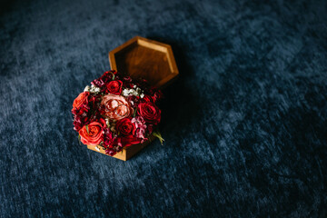 Wooden hexagon ring box with wedding rings and red and pink roses, on deep blue textile background.
