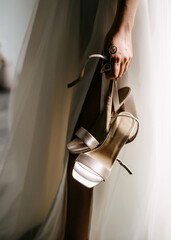 Bride holding elegant wedding shoes, closeup.