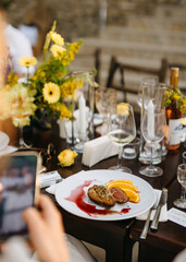 A guest captures a photo of a gourmet dish at a floral adorned table setting.