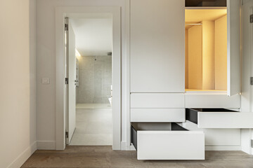 A bedroom with access door to a private bathroom and built-in wardrobe with drawers and open wooden...