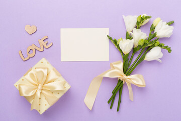 Gift box with freesia flower on color background, top view