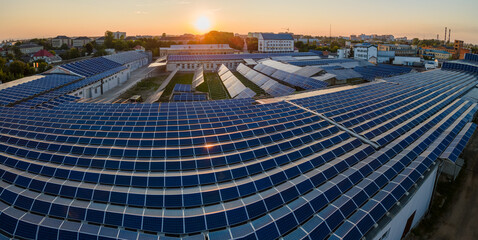 Aerial view of solar power plant with blue photovoltaic panels mounted on industrial building roof for producing green ecological electricity at sunset. Production of sustainable energy concept