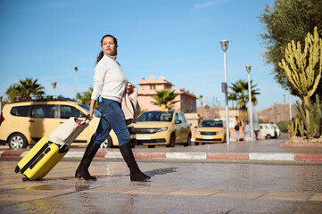 Woman traveler with yellow suitcase, crossing the street on pedestrian crosswalk, confidently...