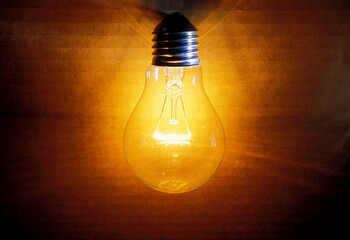 closeup of an old burning light bulb, a carton as background is illuminated, lit with a warm yellow...