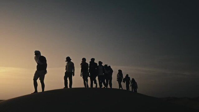 silhouettes of a group of people crossing and walking on a sand dune in the sahara desert in morocco at sunset