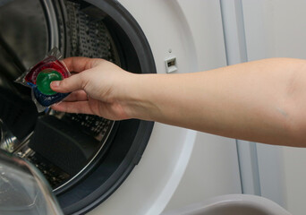 Close up of a woman's hand putting a washing gel pod in a washing machine