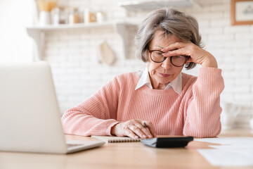Trouble and problems with money. Old elderly senior grandmother woman using laptop calculator for...