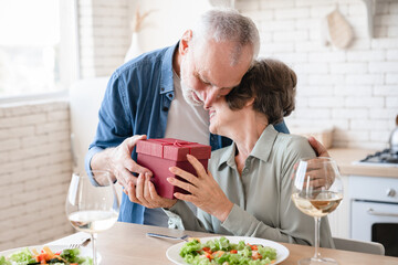 Gratitude love and care concept. Old couple senior spouses celebrating special event birthday anniversary Valentine`s day together, giving presents and gifts at home kitchen