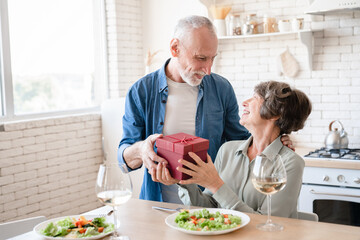 Receiving gifts - love language. Old senior husband giving present gift box to his wife while...