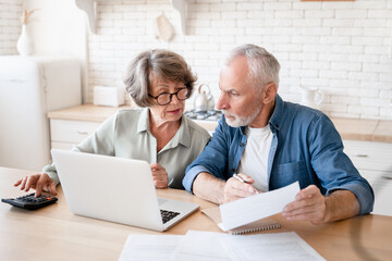 Busy caucasian old elderly senior couple making calculations at home kitchen, checking the...