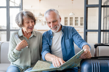 Happy senior old elderly couple spouses grandparents using map, deciding where to go, leaving the country, travelling together on holidays and days off, checking the route with bags and baggage