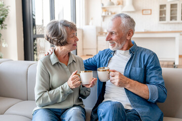 Cheerful old senior elderly couple spouses grandparents drinking tea coffee hot beverage together...