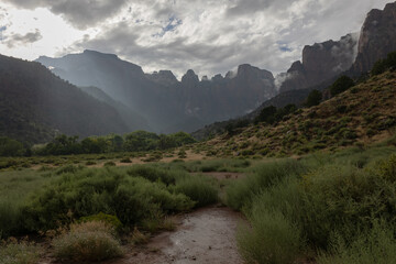 On a rainy September day behind the Human History Museum in Zion Nat. Park, Utah, USA beams of sunlight break through the clouds and slant down over the tops of the red sandstone peak of West Temple.