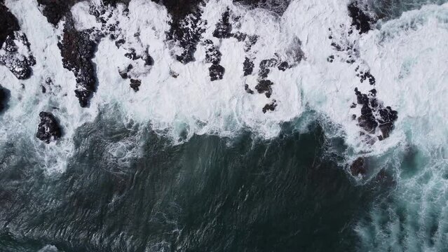 Aerial view captured by drone of large whitecap ocean waves in the Pacific ocean violently crashing into the rocky shore on the coast of Kauai in Hawaii at Spouting Horn.