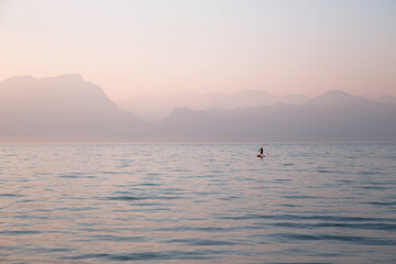 A lonely man standing on an inflatable board with an oar against a backdrop of misty mountains and a lake