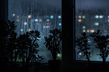 Rain drops on window glass at night evening with town street blurred bokeh blue light. Black...