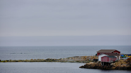 Misty Fog envelopes the homes and weathered boathouses on Fogo Island in Newfoundland-Labrador...