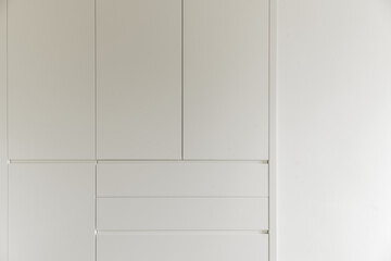 A bedroom with a built-in wardrobe with drawers and white wooden doors and walls painted