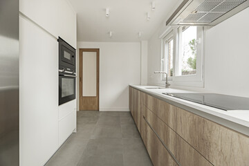 Image of a kitchen with white furniture column and conventional ovens and microwaves, gray stoneware floor