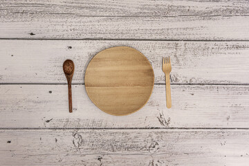 A wooden plate and cutlery of the same material on a light wooden plank surface