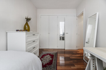 A bedroom with a built-in wardrobe with white wooden doors covering one wall
