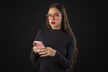 Happy young woman in glasses holding a cell phone on a black background with cinematic lighting