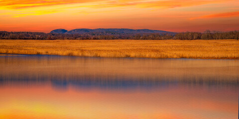 Fototapeta na wymiar Dramatic Sunset over Sleeping Giant Mountain, Gold-colored Common Reeds Plants, and the Quinnipiac River in Hamden viewed from Tidal Marsh Trail in North Haven, Connecticut