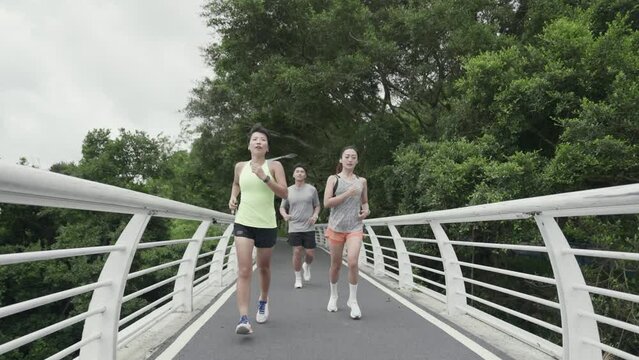 rear view of three young asian people running outdoors in park	