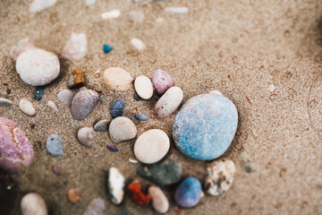 Natural colorful sea round stones on a sandy beach, seashore. Abstract summer holidays background. Ocean shore landscape, seascape. Nature marine.