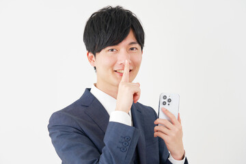 スマートフォンを持って内緒のジェスチャーをするビジネスマン　白背景