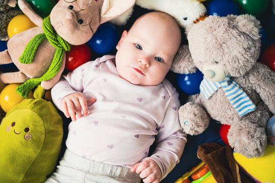 top view of cute infant baby girl lying on floor among colorful toys