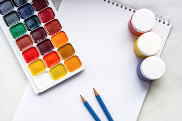 Colorful watercolor or acrylic paints and pencils on a white sheet of paper on a white background. Design studio table top view. Space for text.
